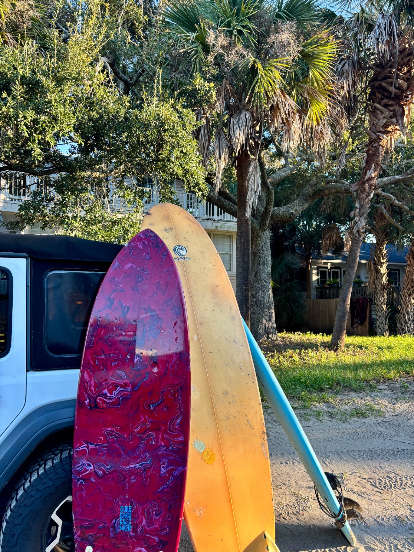 Marbled pink and orange longboards leaning against a Jeep in the sand