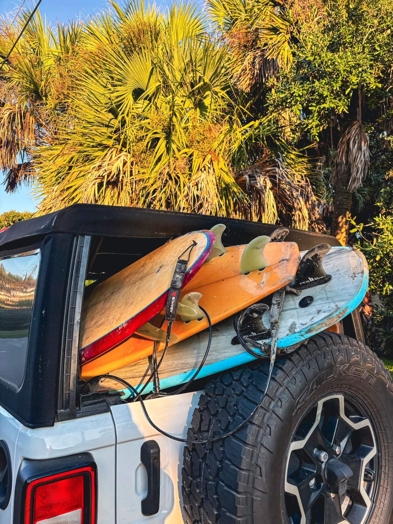 Three surfboards stacked through the back of a Jeep with palms overhead